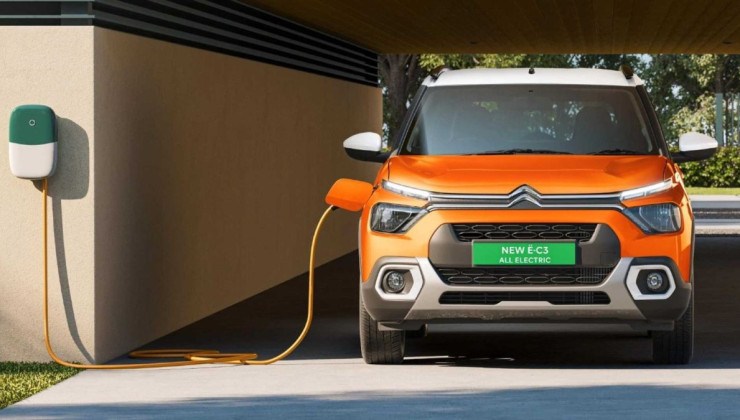 Citroen C3 el&eacute;trico laranja visto de frente sendo recarregado em tomada dom&eacute;stica.