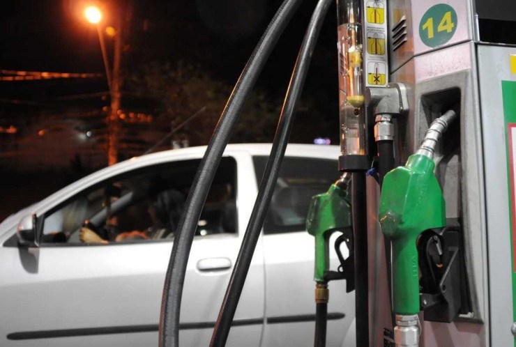Bomba de etanol em primeiro plano, à direita, com carro prata ao fundo em posto de combustíveis