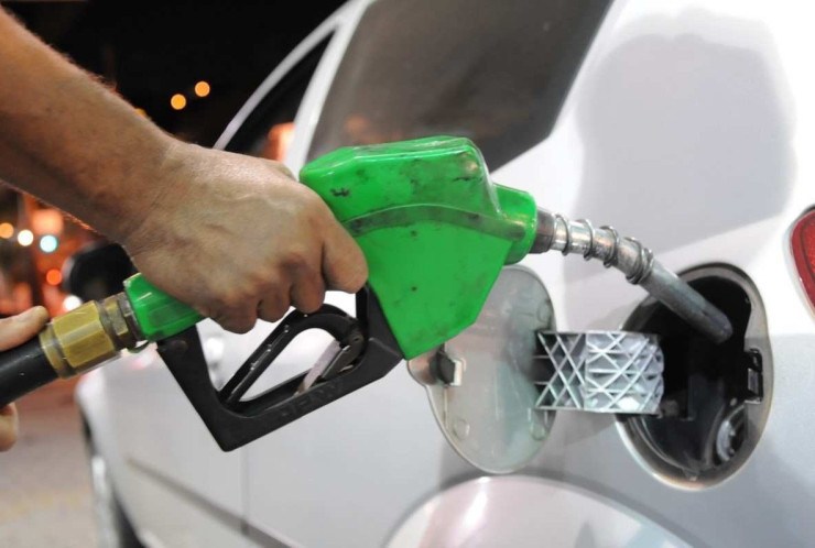 Bico de bomba de etanol sendo colocada no bocal do tanque de ve&iacute;culo prata em posto de combust&iacute;veis.