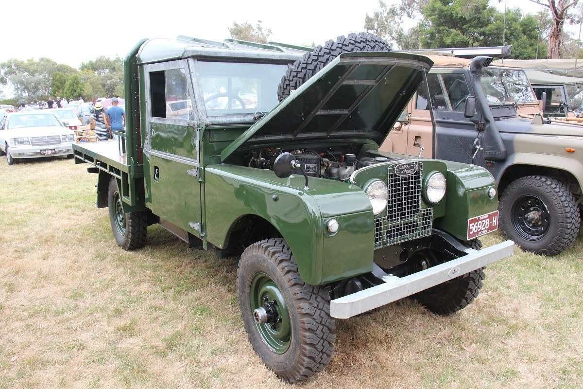 1955 Land Rover Series I 86 na cor verde está com seu capô aberto em um campo de grama. 