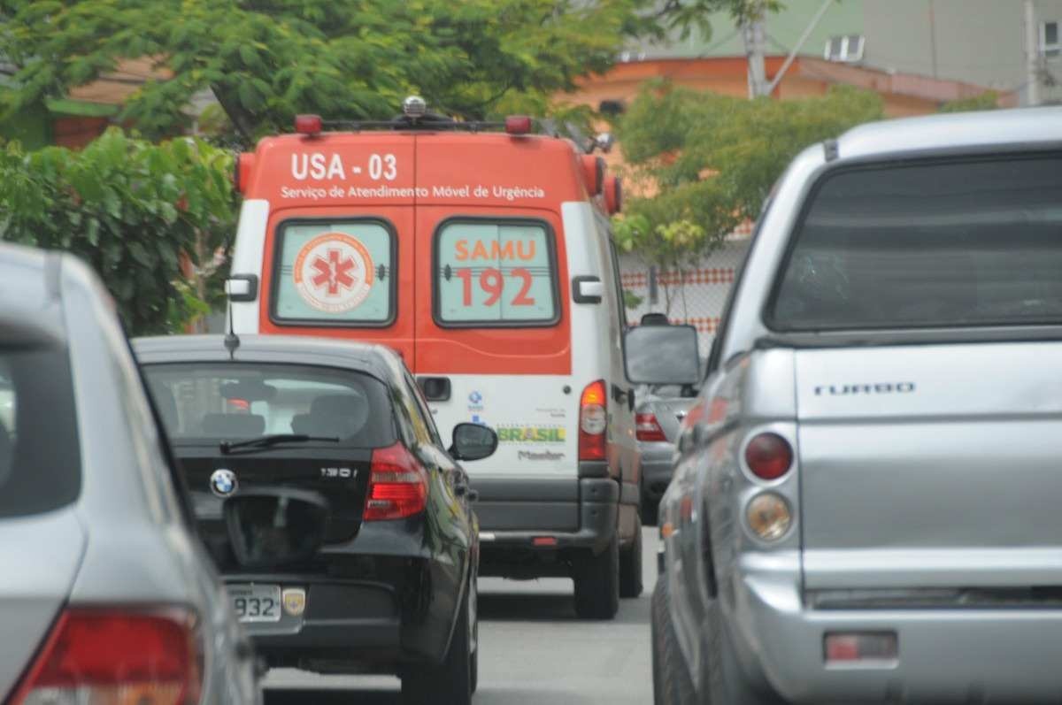 Veículos no trânsito em avenida com uma ambulância ao fundo