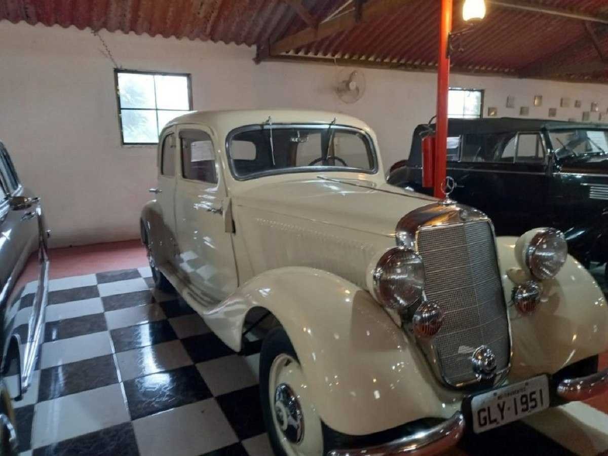 Mercede-Benz de 1951 exposta em museu, o veículo está estacionado em uma chão xadrez preto e branco, atrás é possível ver uma parede na cor creme com uma janela e ventilador.