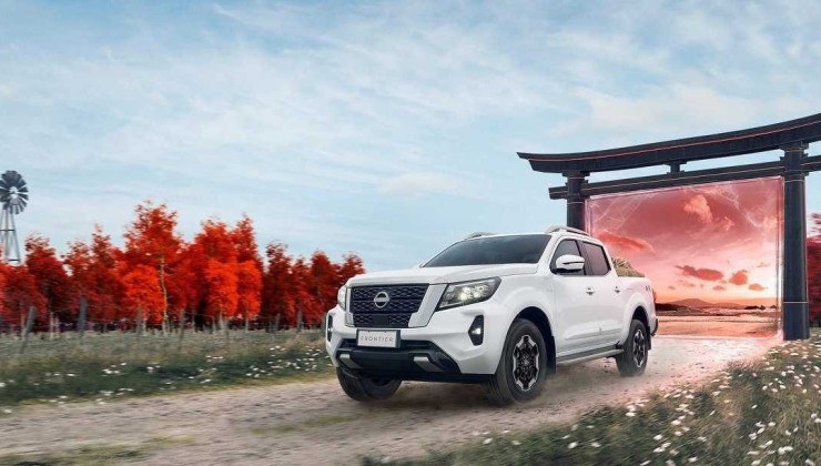 Nissan Frontier em estrada de terra com grama ao fundo e árvores de folhas vermelhas.