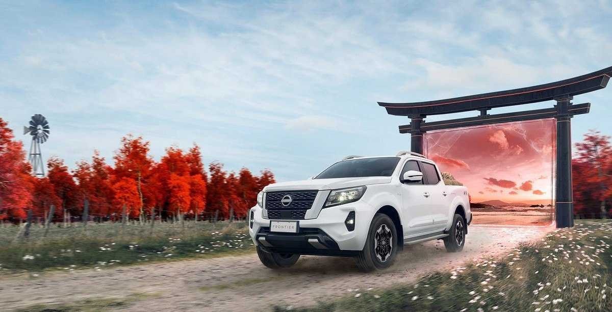 Nissan Frontier em estrada de terra com grama ao fundo e árvores de folhas vermelhas.