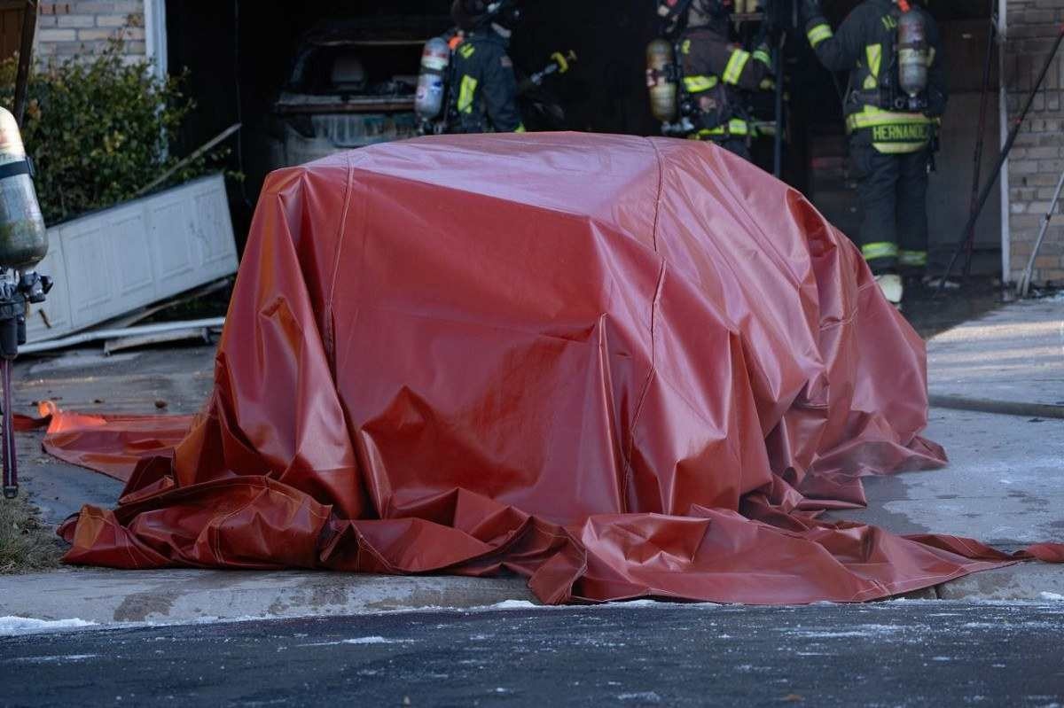 Capa vermelha sobre carroceria de veículo com bombeiros ao fundo