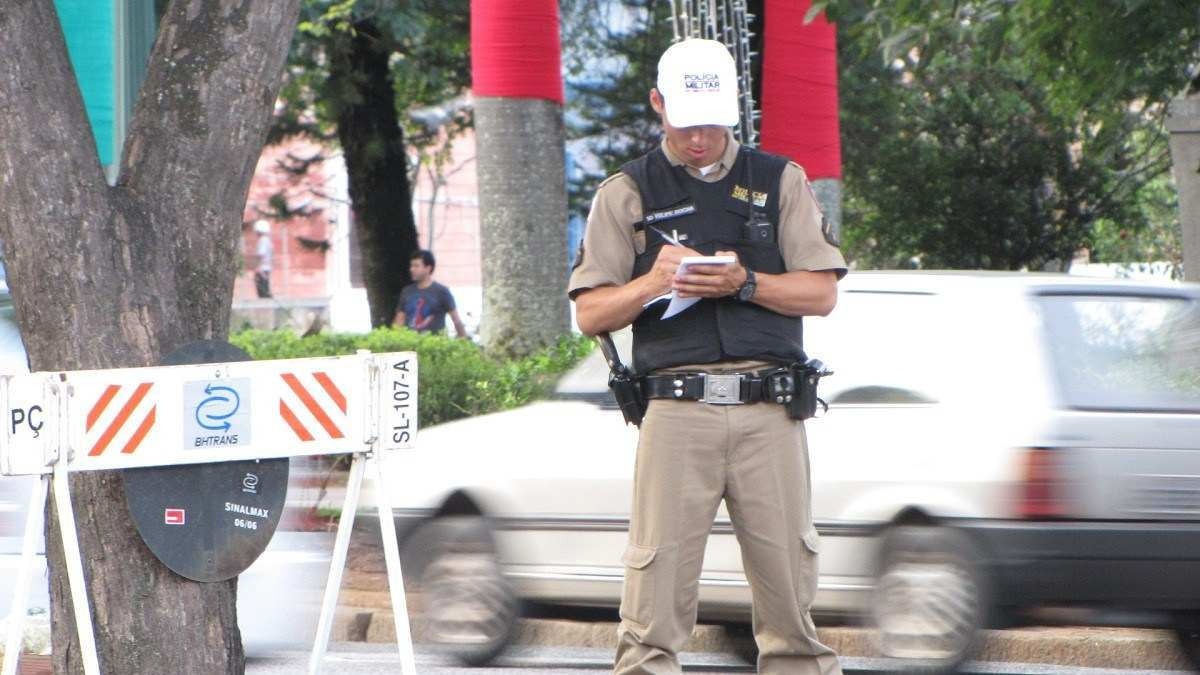 policial fazendo registro de multa com carro passando ao fundo