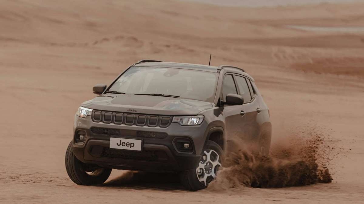 Jeep Compass em deserto de areia visto pela dianteira e jogando areia para o alto.