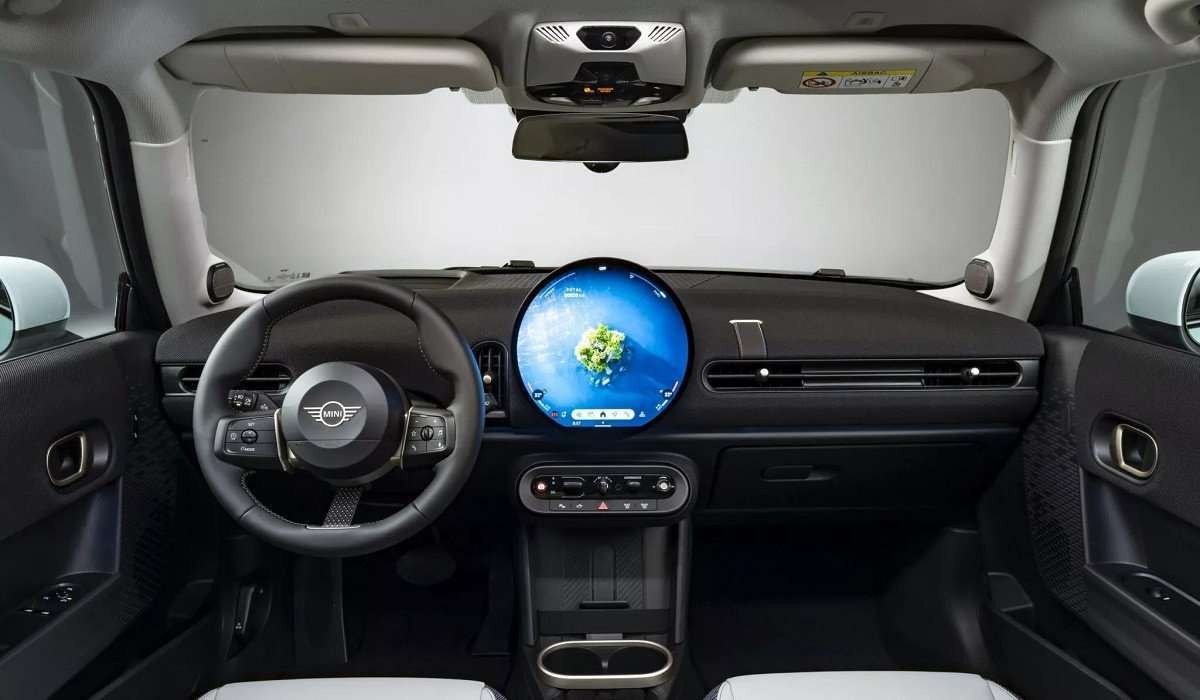 Interior do Mini Cooper com tela OLED ligada ao centro e fundo branco visto pelo para-brisa.