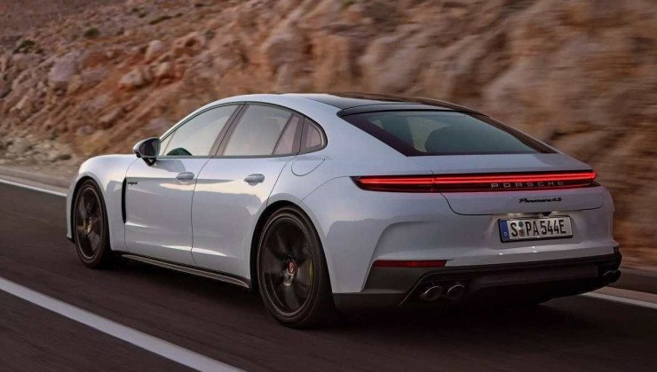 Porsche 4S E-Hybrid branco visto trafegando em estrada pavimentada e ao fundo uma parede de pedras.
