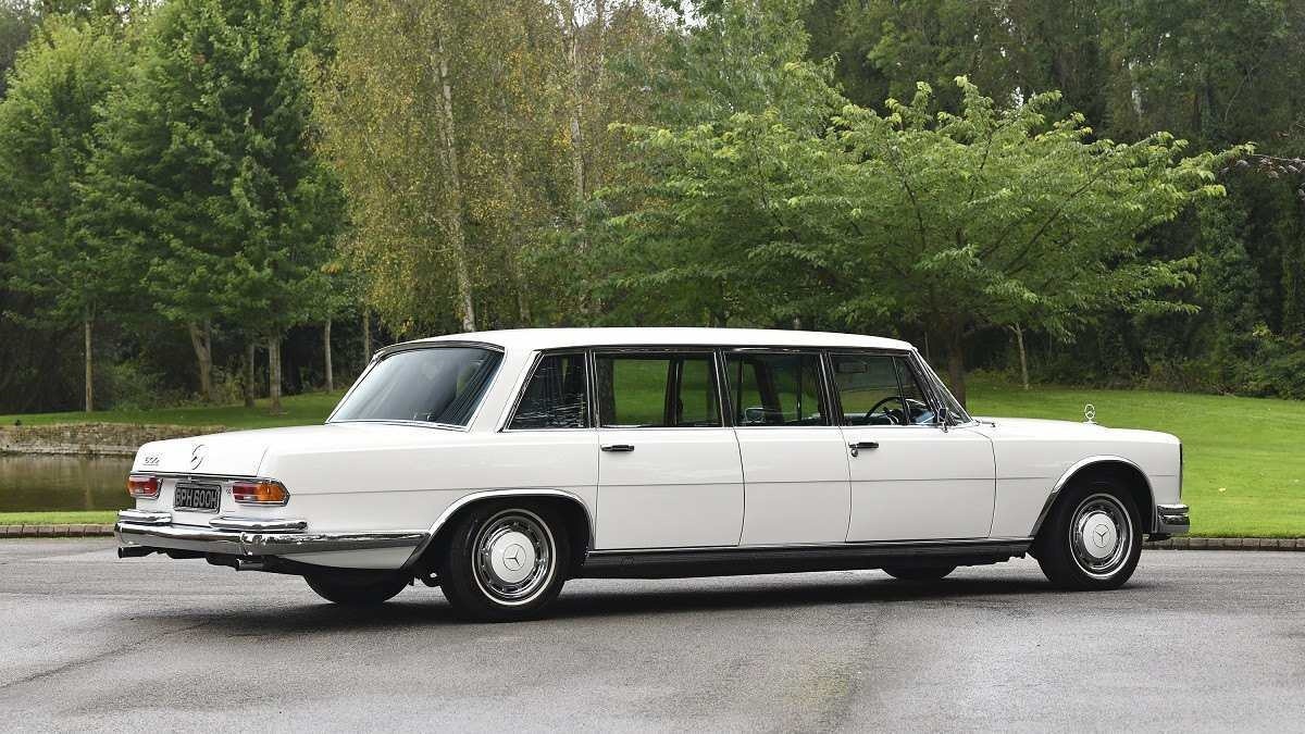 Mercedes-Benz 600 Pullman branca vista lateralmente em chão pavimentado com chão gramado e árvores ao fundo.