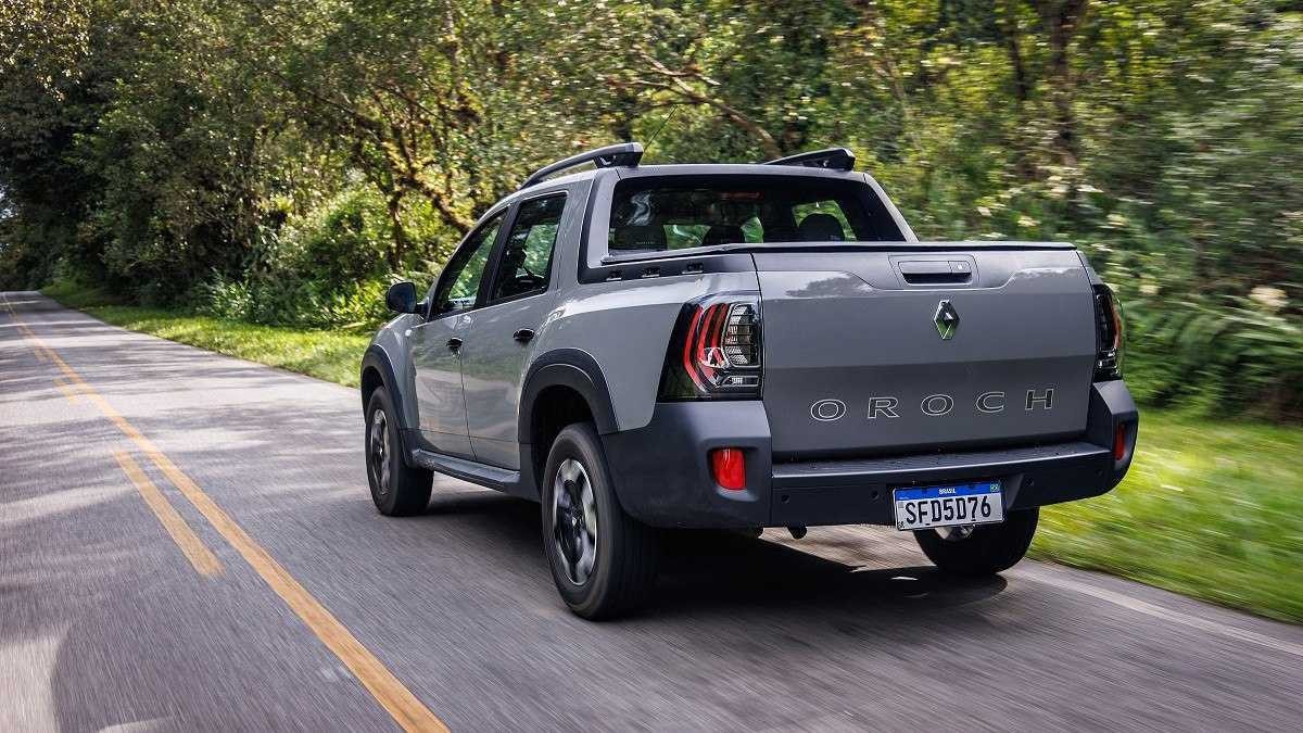 Renault Oroch cinza visto pela traseira em estrada pavimentada e árvores ao fundo.