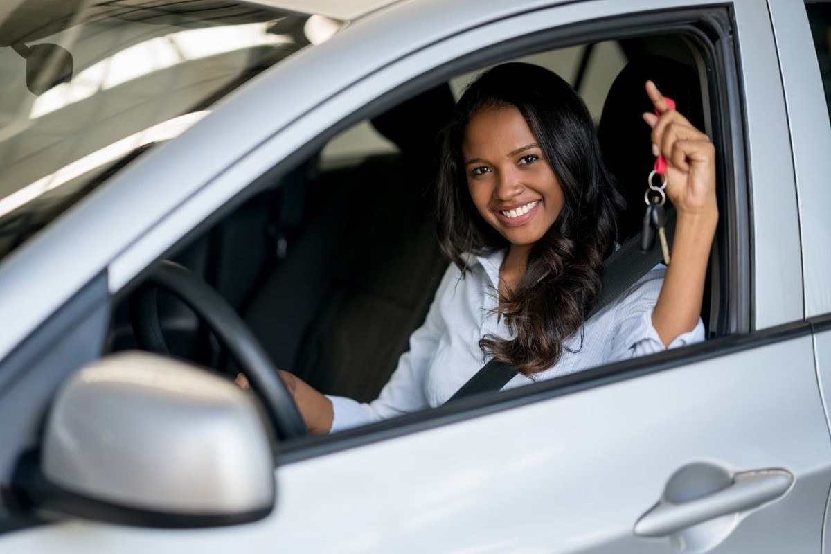 Mulher motorista segurando a chave dentro de um carro de cor prata