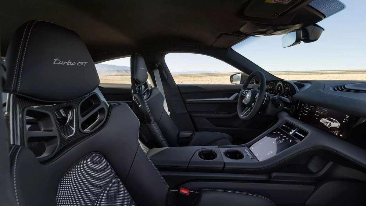 Interior do Porsche Taycan Turbo GT em preto, os bancos possuem escrito 'Turbo GT' no encosto de cabeça. É possível enxergar o céu azul pelas janelas e para-brisas.