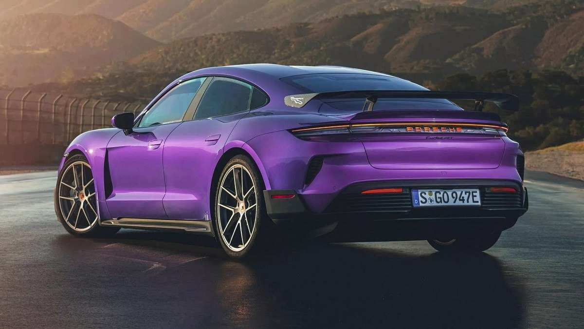 Porsche Taycan Turbo GT roxo visto pela traseira em pista pavimentada com montanha ao fundo e reflexo de luz no canto esquerdo superior.