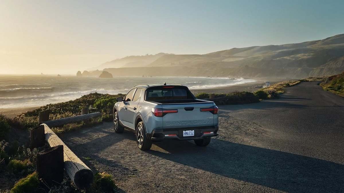 Hyundai Santa Cruz visto pela traseira em rodovia próximo a ponta de penhasco, ao fundo é possível ver água e montanha com céu claro e amarelado.