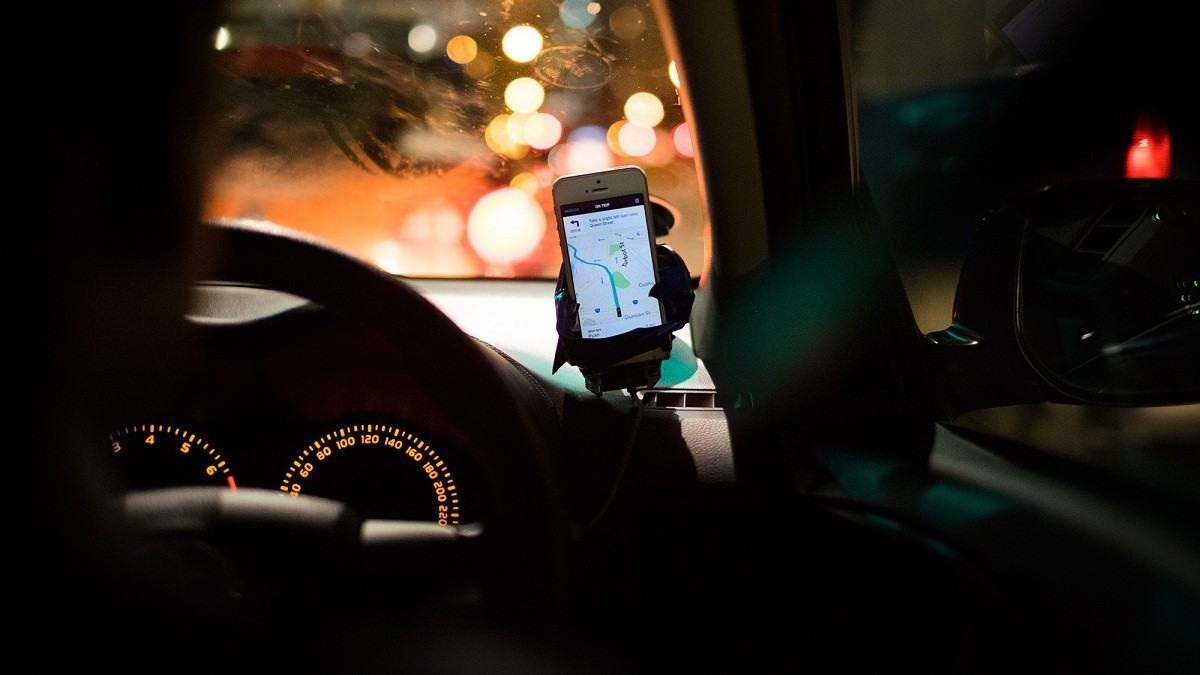 Motorista com celular grudado no para-brisa com aplicativo da Uber aberto.
