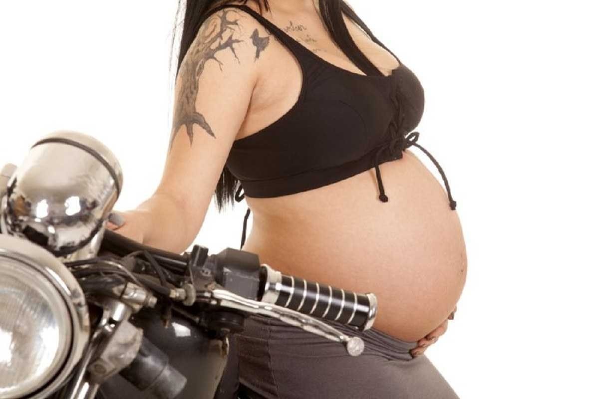 Mulher grávida de barriga de fora ao lado de uma moto