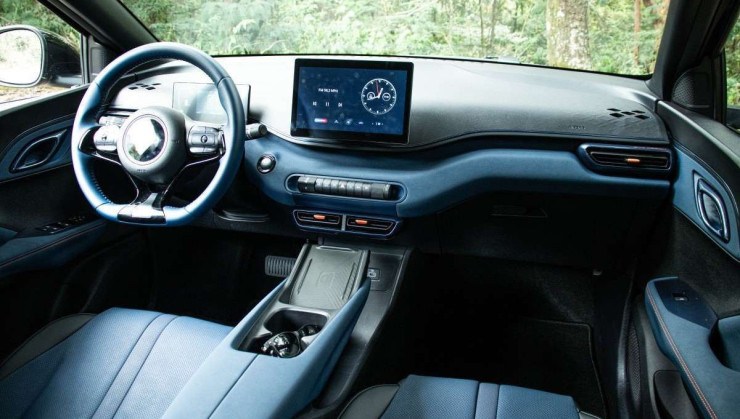 Interior do BYD Dolphin Mini com acabamento em preto. Pelo para-brisas é possível ver pequeno morro coberto por árvores de folhagem verde clara