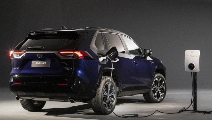 Toyota RAV4 XSE Plug-in Hybrid azul escuro visto pela traseira sendo carregado por wallbox, ao fundo há uma parede preta.