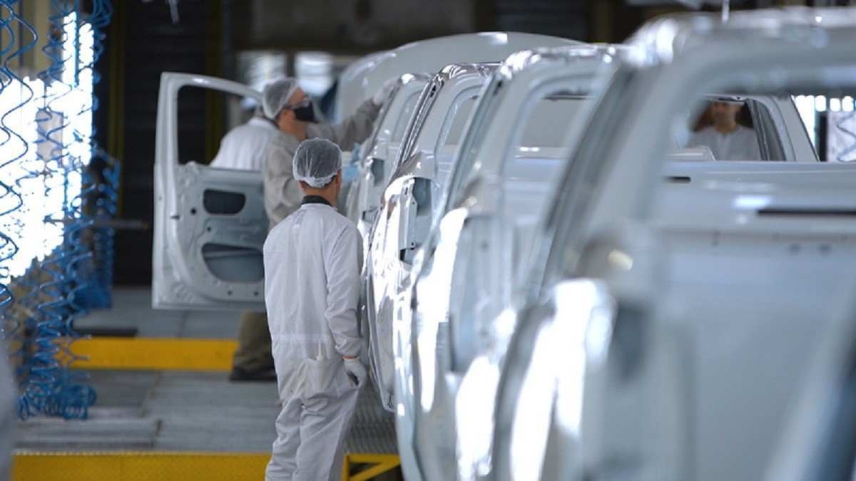 Linha de produção da Mitsubishi com uma pessoa ao fundo de fone de ouvido de proteção com várias carrocerias brancas ao lado direito
