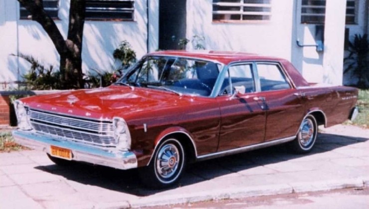 Ford Galaxie Landau vermelho visto lateralmente em frente a uma casa de paredes brancas e uma &aacute;rvore no canto esquerdo ao fundo.