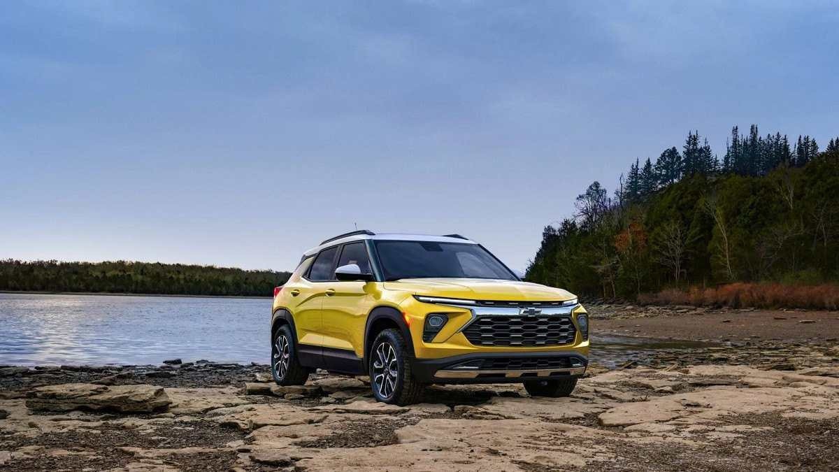 Chevrolet TrailBlazer amarelo sobre chão de pedras com lago ao fundo, árvores com folhagens verde escuro ao lado direito e céu claro ao fundo