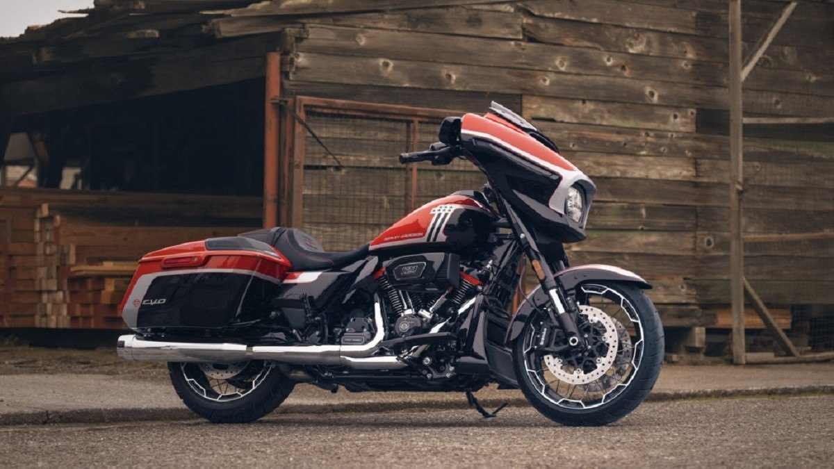 Harley-Davidson CVO Street Glide vermelha com detalhes em preto está parada em chão de terra com curral ao fundo