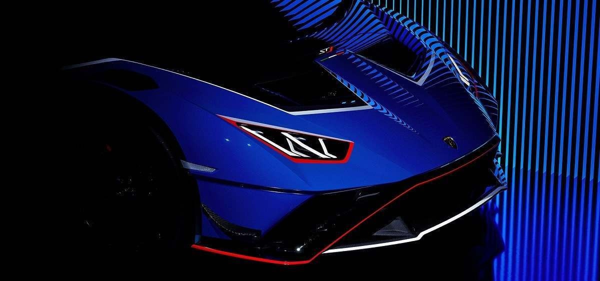 Lamborghini Huracan STJ azul e detalhes em branco e vermelho está parado em frente a telão de LED azul, a foto dá foco a dianteira do modelo