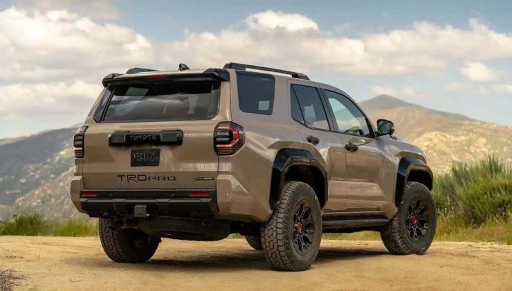 Toyota 4Runner marrom visto pela traseira com detalhes da lateral em estrada de terra com arbustos no canto direito, montanha e céu claro com nuvens ao fundo.