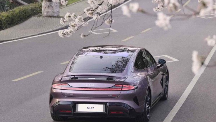 Carro Xiaomi SU7 visto de trás e de cima, rodeado de flores no topo de uma árvore