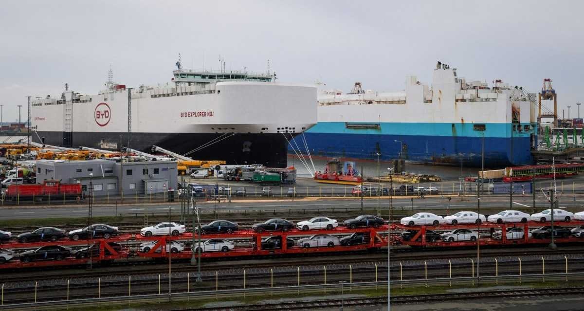 Dois navios de transporte de veículos, um deles da marca BYD, descarregam no porto de Bremerhaven, na Alemanha; em primeiro plano, vê-se vagões ferroviários transportando os automóveis