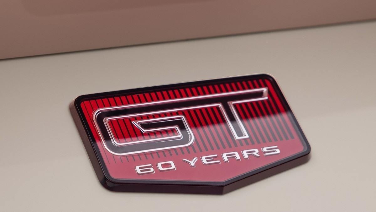 Emblema vermelho com as palavras "GT 60 YEARS" em carroceria de Ford Mustang branco.