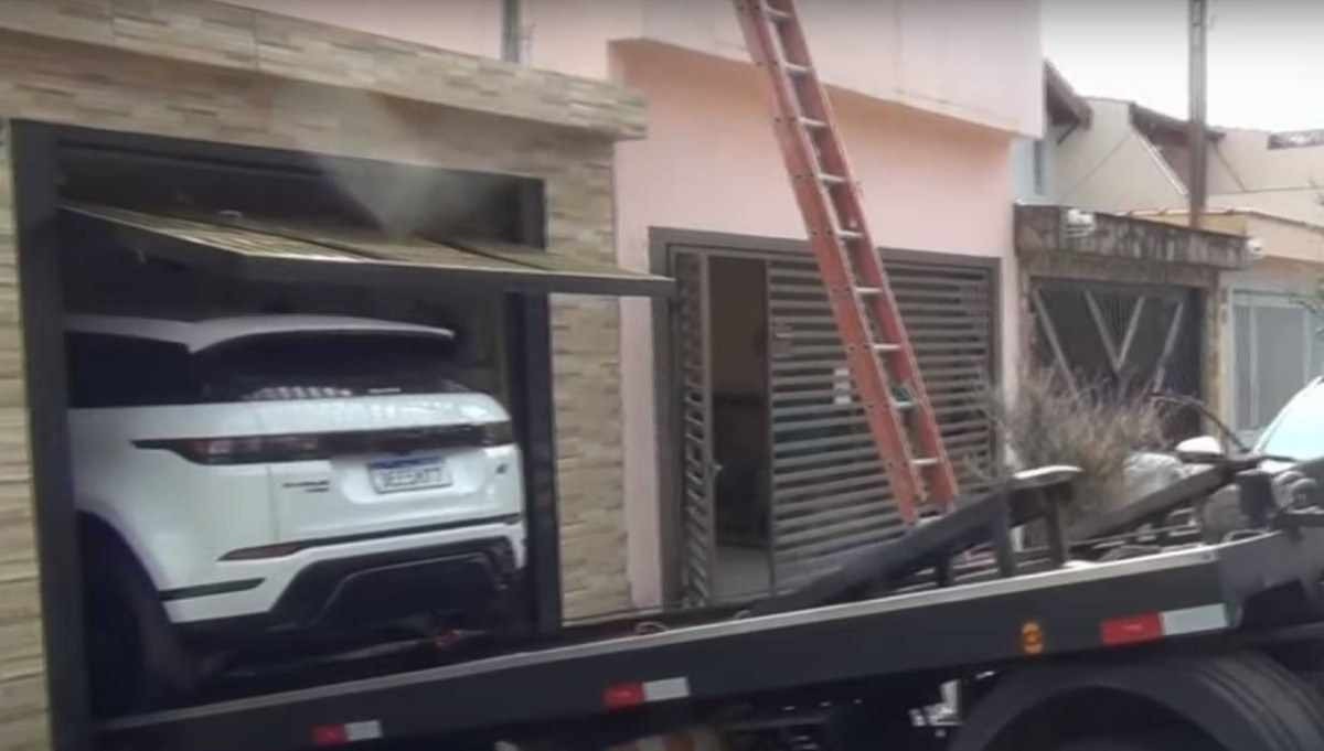 Carro de luxo Range Rover Evoque sendo rebocado de garagem residencial durante apreensão judicial; veículo teria sido tomado do jogador do Palmeiras Dudu