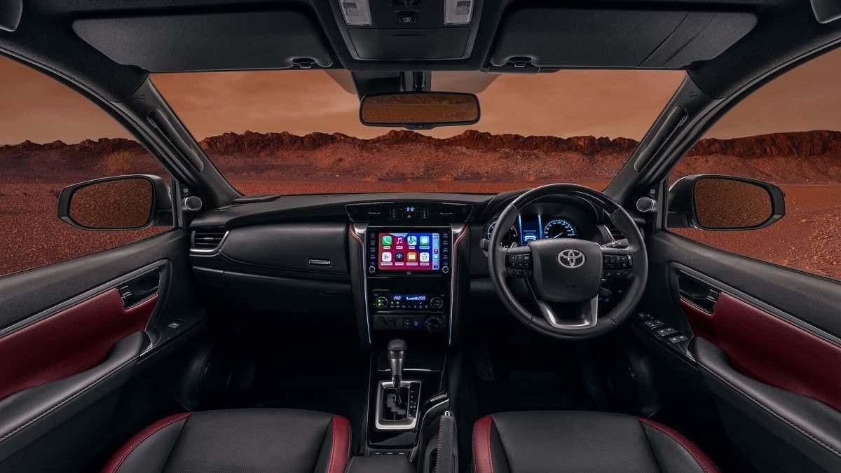 Interior do Toyota SW4 MHEV com bancos e acabamento em preto com detalhes vermelhos, pelo para-brisa e janelas do motorista e passageiro é possível observar chão rochoso vermelho que simula Marte