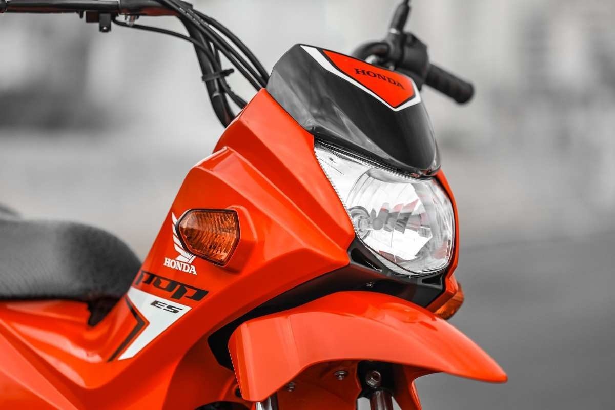 Honda Pop 110i modelo 2025 na cor vermelha detalhe do farol para-lama e guidão estática no asfalto