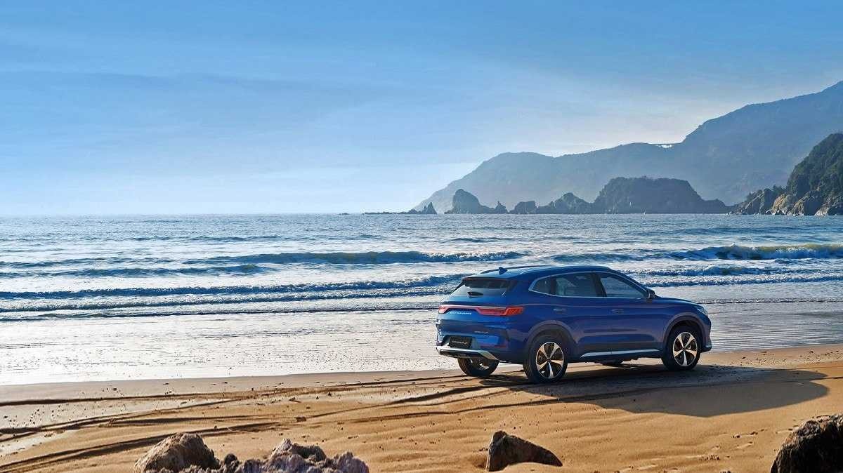 BYD Song Plus visto pela traseira com detalhes da lateral em praia. Ao fundo é possível ver montanhas no lado direito e céu claro com poucas nuvens ao lado.