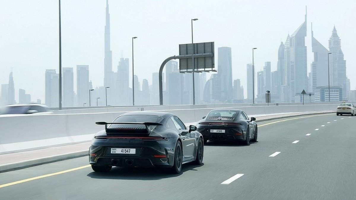Porsche 911 híbrido preto na estrada asfaltada com cidade ao fundo 