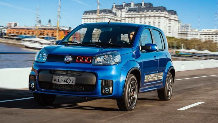 Fiat Uno Sporting 1.4 2015 azul, de frente, em movimento por via urbana, com prédios históricos ao fundo