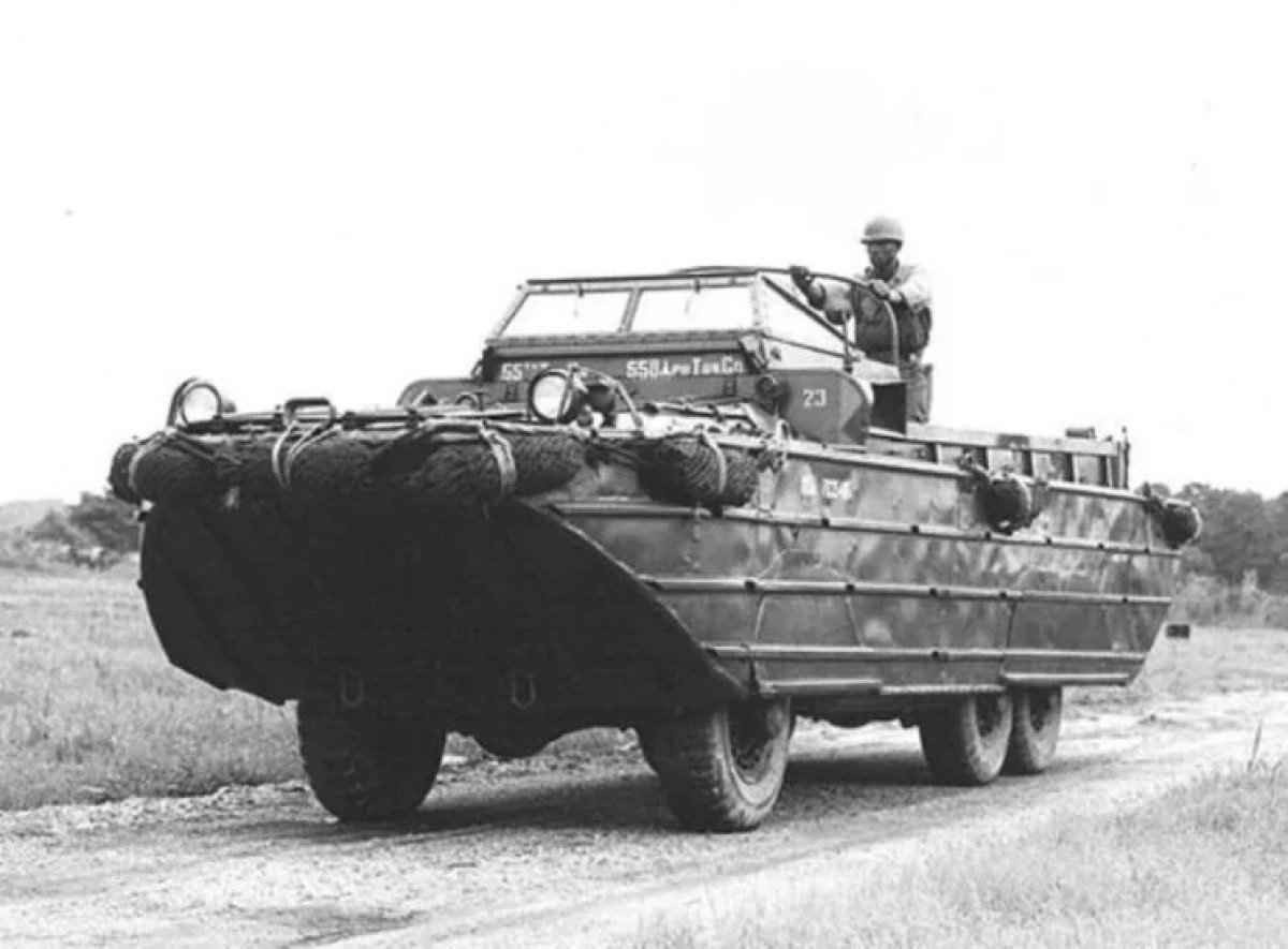 DUKW 6x6 em preto e branco viaja em uma estrada de terra com um soldado em cima do corpo