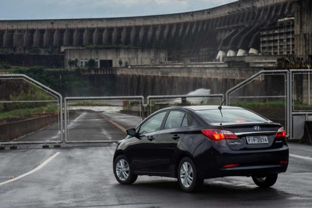 Hyundai HB20S modelo 2013 preto de traseira estático no asfalto prédio ao fundo.jpg