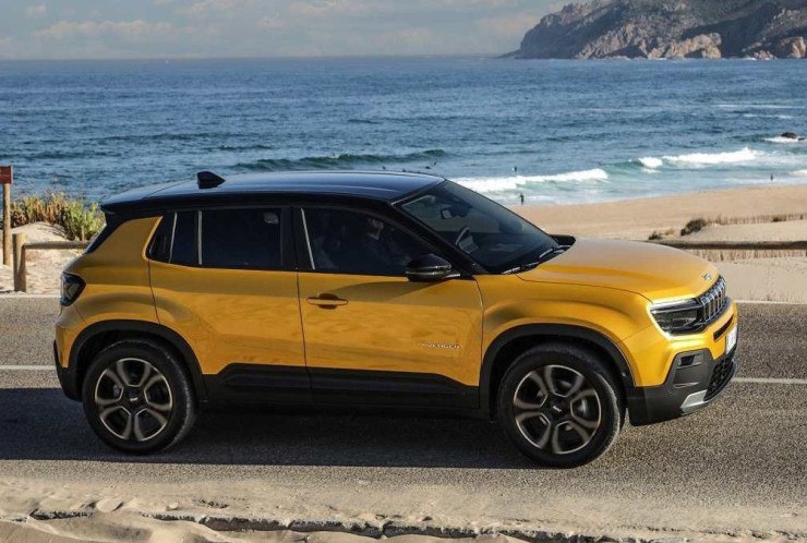 Jeep Avenger amerelo visto pela lateral trafega em rodovia pavimentada. Ao fundo &eacute; poss&iacute;vel ver praia de areia clara com mar calmo ao lado. Em &uacute;ltimo plano &eacute; poss&iacute;vel enxergar penhasco e c&eacute;u claro.