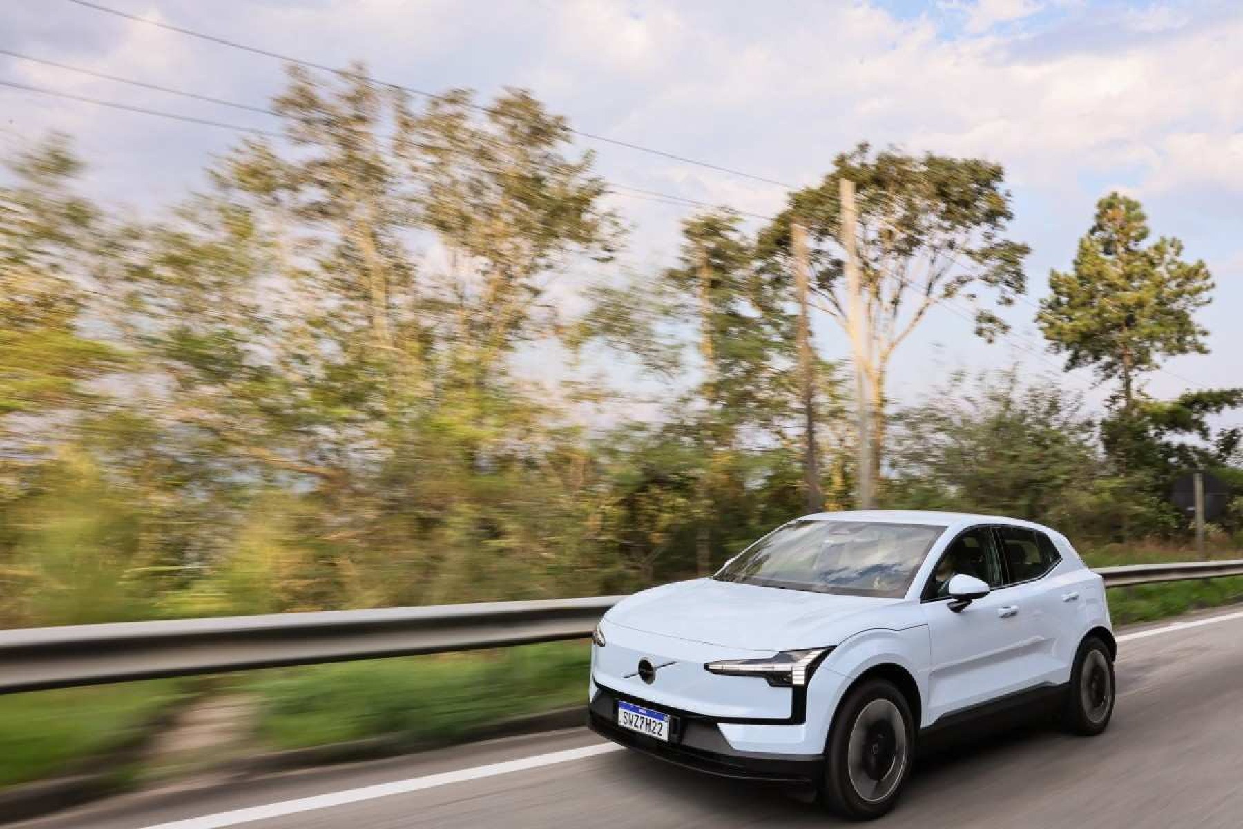 Volvo EX30 branco de frente em movimento em estrada asfaltada com mata ao fundo