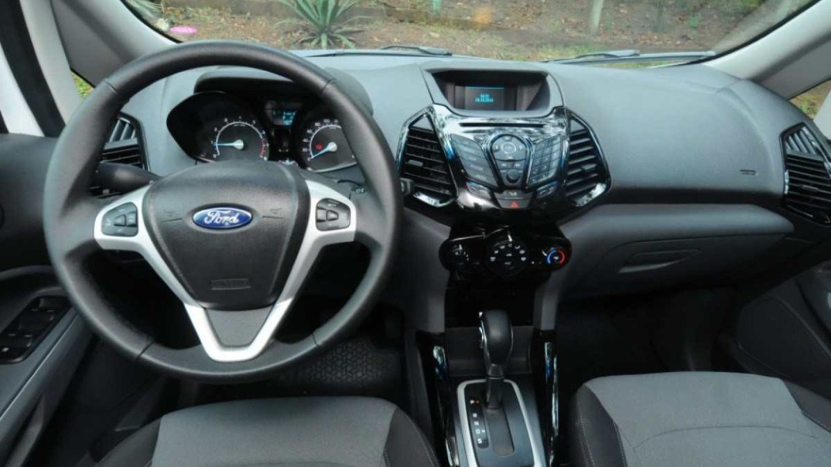 Ford EcoSport Freestyle 1.6 modelo 2015 interior branco painel volante bancos dianteiros estáticos no asfalto com plantas ao fundo