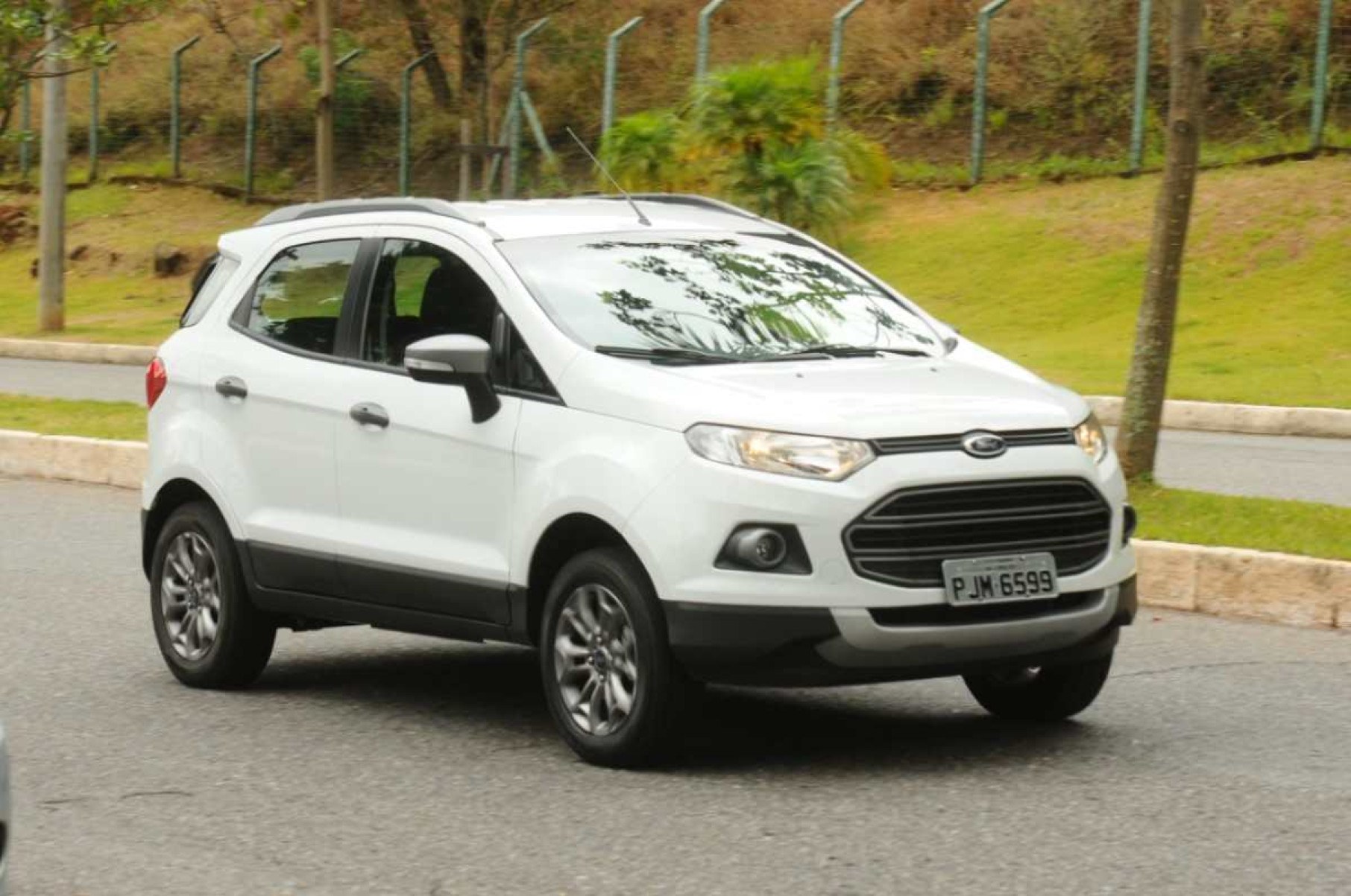 Frente do modelo Ford EcoSport Freestyle 1.6 branco 2015 movendo-se no asfalto com plantas ao fundo