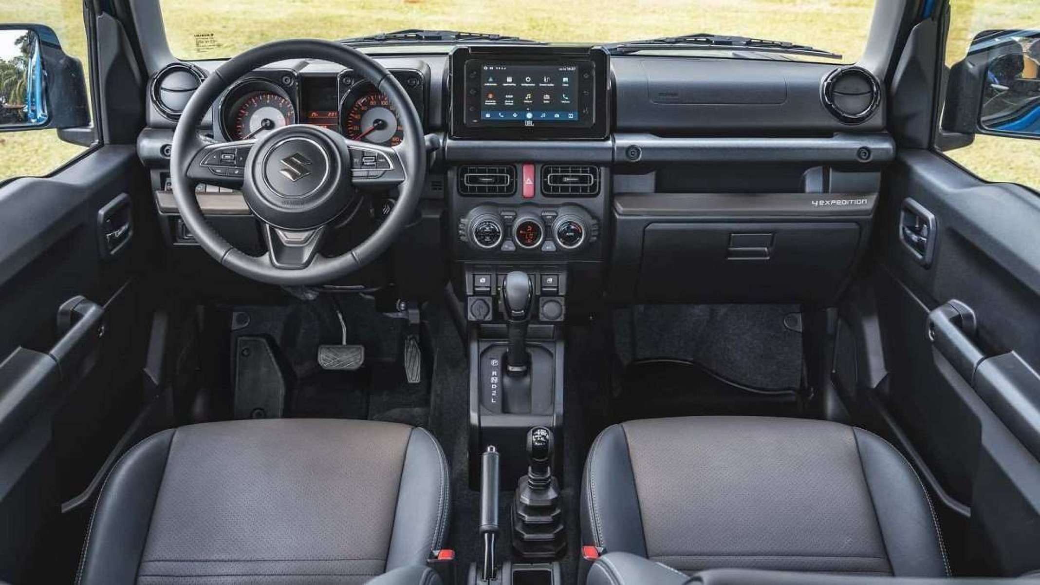 Interior do Suzuki Jimny Sierra 4Expedition com interior preto. Pelo para-brisas e janelas laterais &eacute; poss&iacute;vel ver campo gramado.