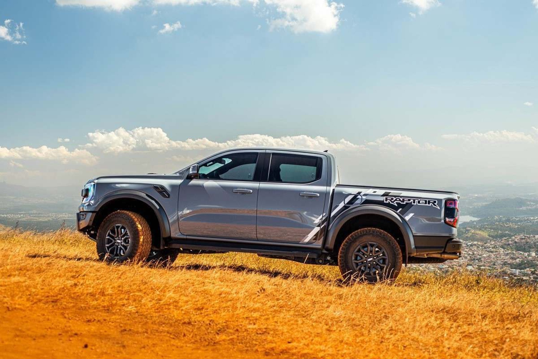 Ford Ranger Raptor 2024 cinza, de lateral, estacionada em campo