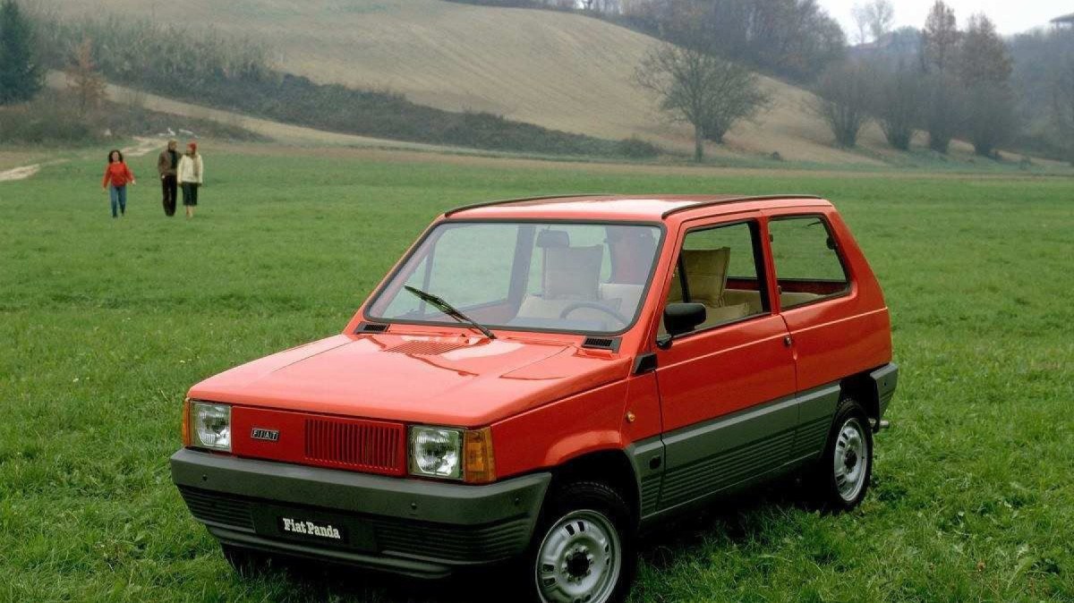 Fiat Panda 1980, vermelho, de frente, estacionado em campo gramado, com montanhas ao fundo e céu nublado
