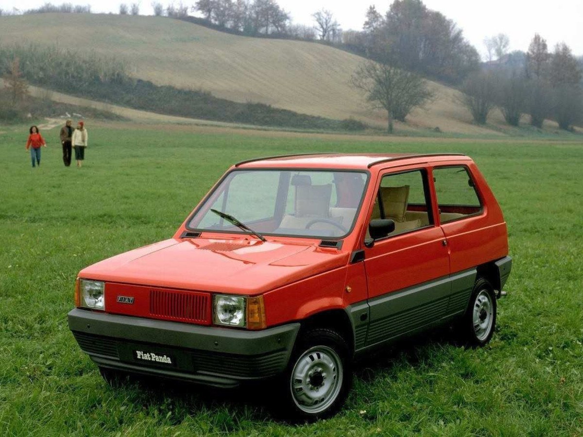 Fiat Panda 1980, vermelho, de frente, estacionado em campo gramado, com montanhas ao fundo e céu nublado