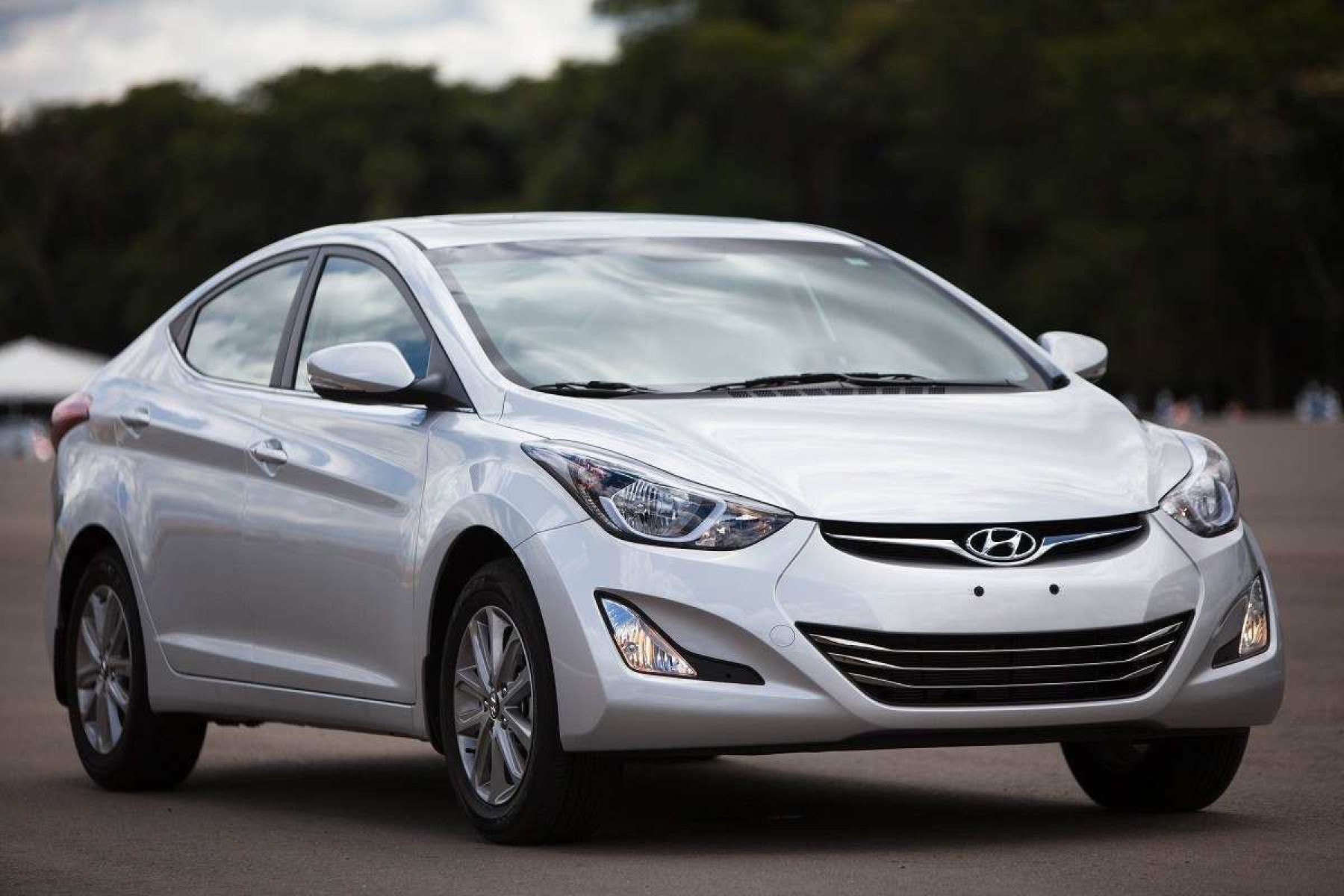 Hyundai Elantra 2014 prata, de frente, estacionado em local asfaltado, com vegetação ao fundo 