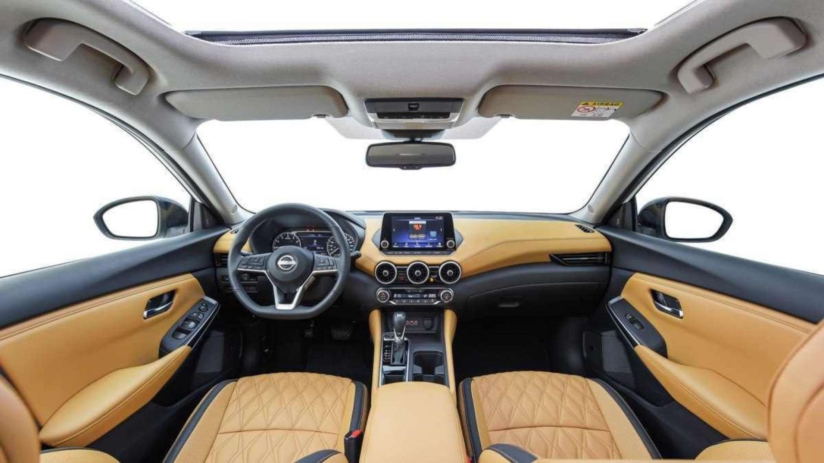 Interior do Nissan Sentra Exclusive 2025 com interior caramelo e detalhes em preto. Fundo branco é visto por teto-solar, para-brisa e janelas laterais.